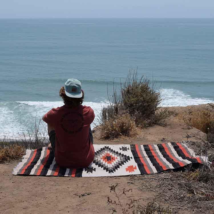 Man sitting on striped and diamond pattern blanket overlooking beach